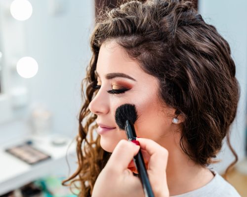 Make up artist applying professional make up to beautiful young woman.